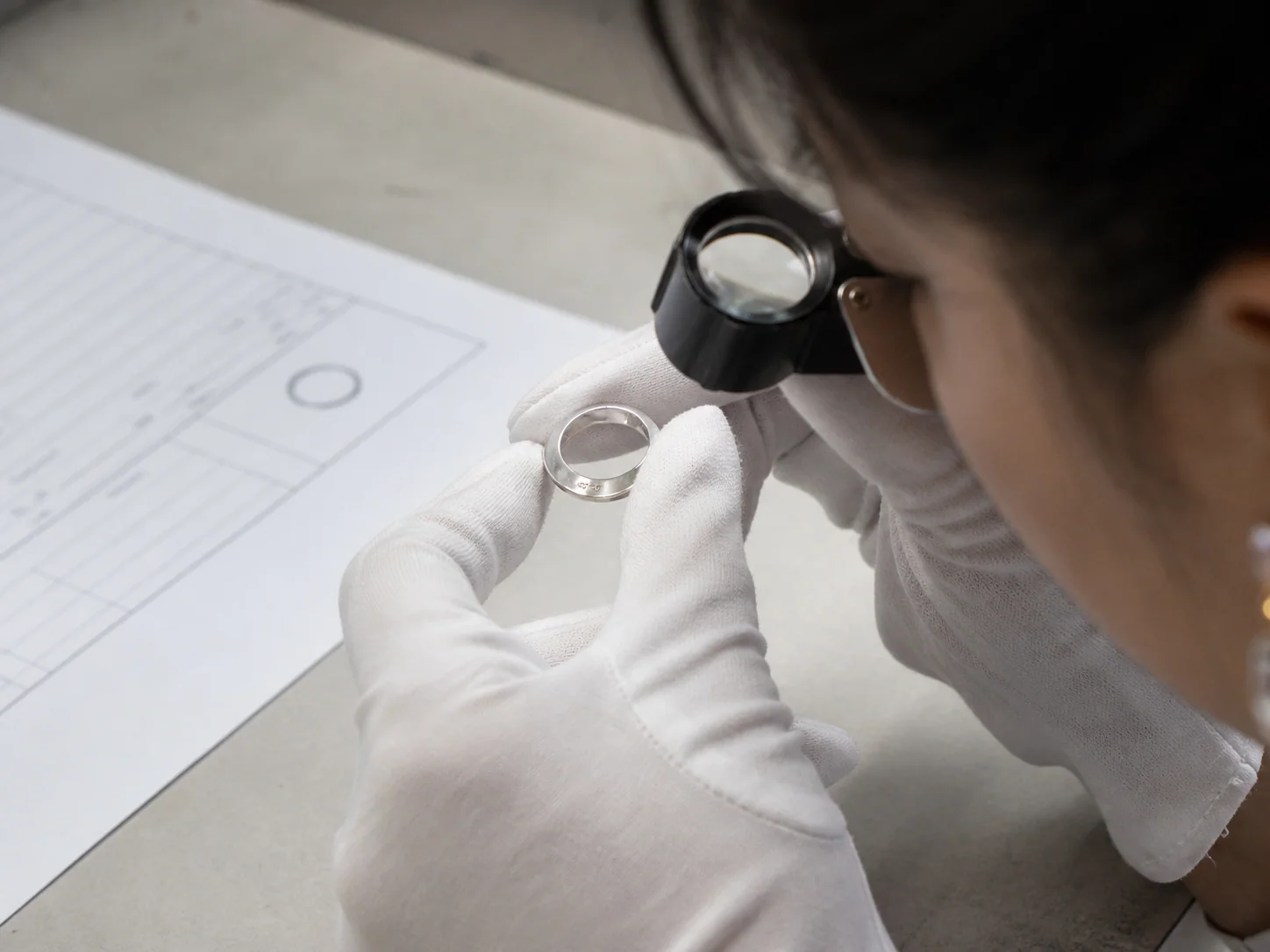 A finished silver ring's inside marking being checked against an order sheet