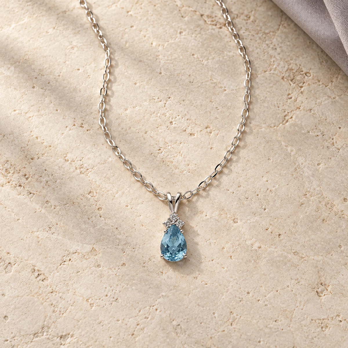 Blue pear-shaped pendant necklace styled on an ivory stone surface